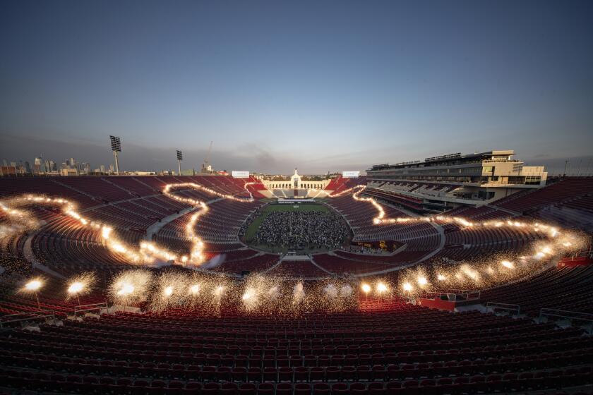 Blasts of low fireworks are set off in the L.A. Memorial Coliseum, ringing the audience standing on the field.