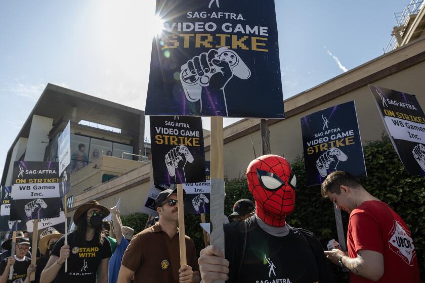 A person in a Spider-Man mask marching in a group of people carrying picket signs that read 'SAG-AFTRA video game strike'