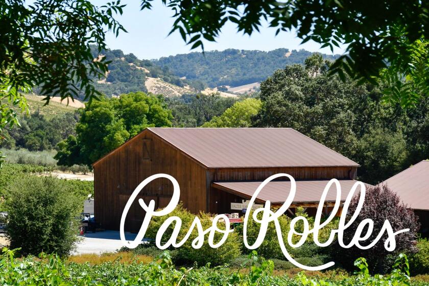 Photo of vineyard with rolling green hills and trees, with a brown wooden building for wine tasting.