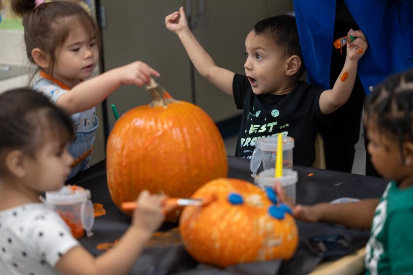 Four children sit around a table painting pumpkins.