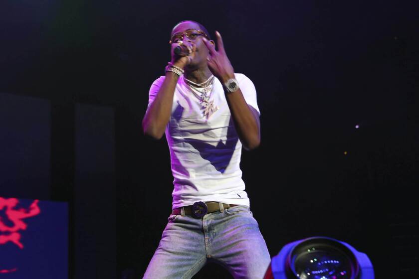 Rich Homie Quan in skinny jeans and a white shirt rapping on a stage. He holds a microphone in his right hand 