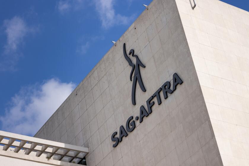 The SAG-AFTRA logo on a gray building against a sunny sky with clouds.