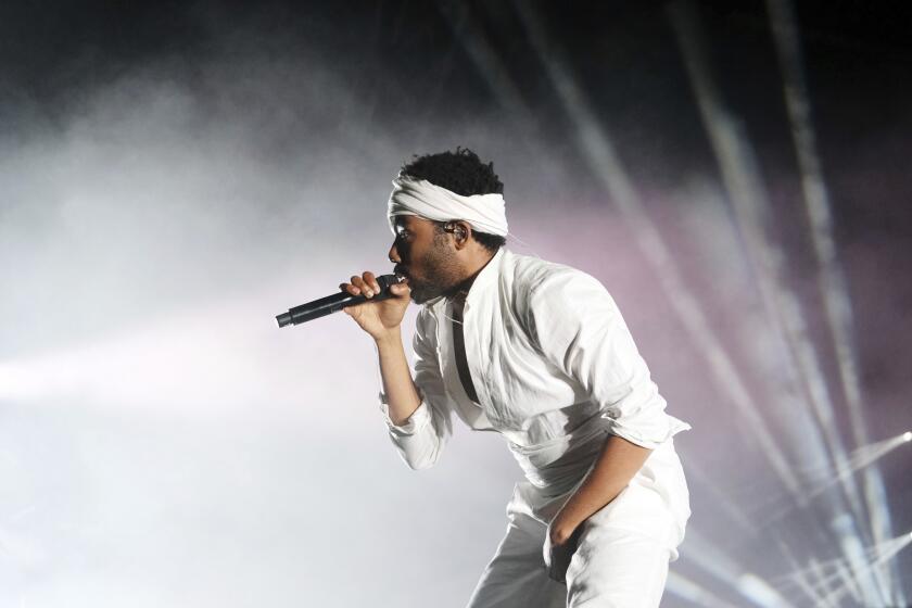 Donald Glover in a white outfit and a white headband singing on a stage