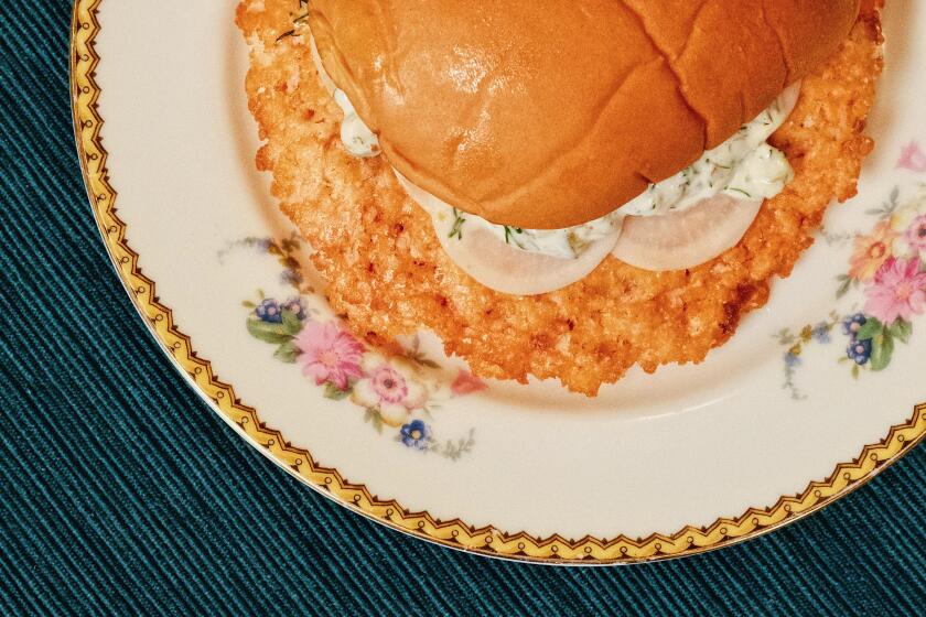 An overhead of a salmon smash burger with turnips and white sauce on a flowered china plate on a deep blue placemat.