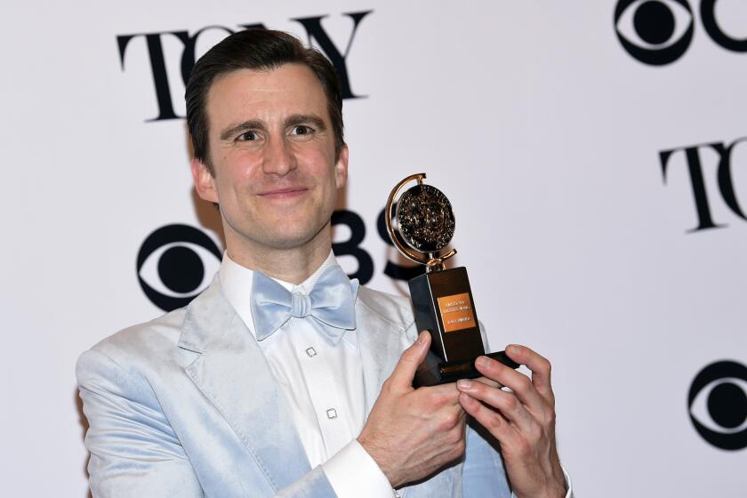 Gavin Creel wears a light blue blazer as he holds up his Tony Award