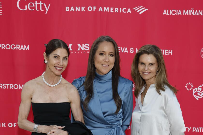 Three women in formalwear stand in front of a red background and pose for a photo