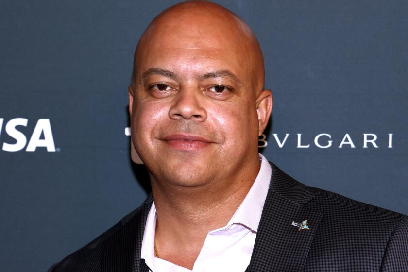 Jon-Adrian Velazquez wearing a suit without a tie posing against a gray background with white text